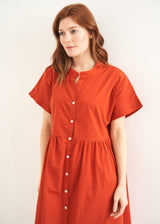 A model wearing a oversized shirt dress in a rusty red tone with mother of pearl buttons