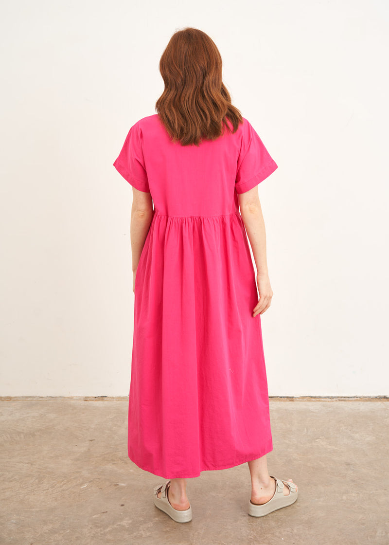 A model wearing a bright pink midaxi shirt dress with short sleeves and mother of pearl buttons