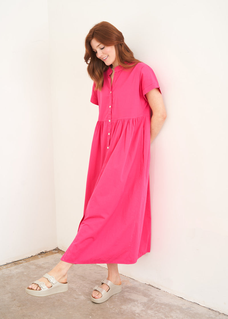 A model wearing a bright pink midaxi shirt dress with short sleeves and mother of pearl buttons