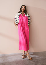 A model wearing a bright pink midaxi shirt dress with short sleeves and mother of pearl buttons