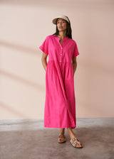 A model wearing a bright pink midaxi shirt dress with short sleeves and mother of pearl buttons