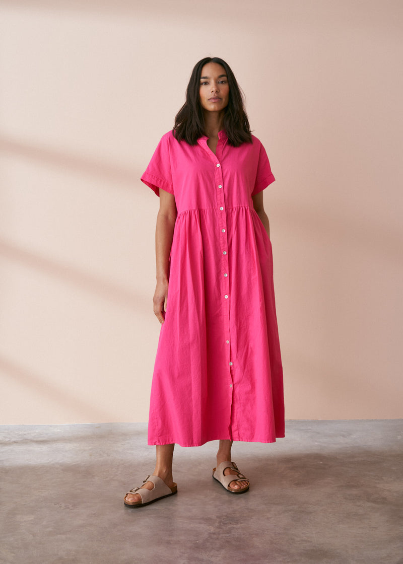 A model wearing a bright pink midaxi shirt dress with short sleeves and mother of pearl buttons