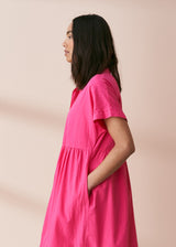 A model wearing a bright pink midaxi shirt dress with short sleeves and mother of pearl buttons