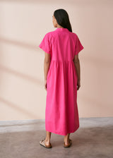 A model wearing a bright pink midaxi shirt dress with short sleeves and mother of pearl buttons