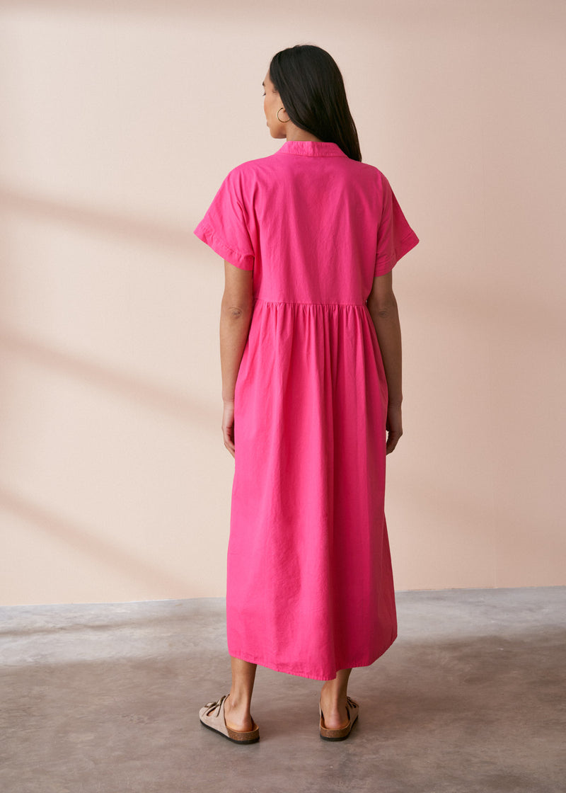 A model wearing a bright pink midaxi shirt dress with short sleeves and mother of pearl buttons