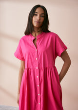 A model wearing a bright pink midaxi shirt dress with short sleeves and mother of pearl buttons