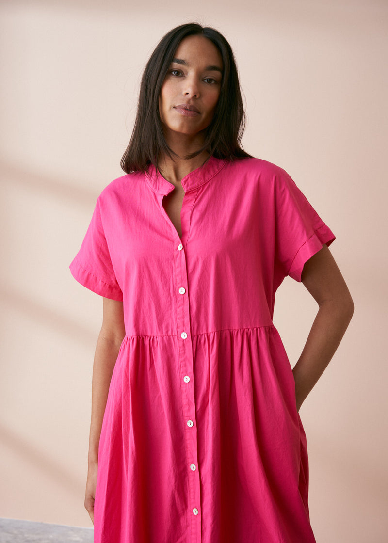 A model wearing a bright pink midaxi shirt dress with short sleeves and mother of pearl buttons