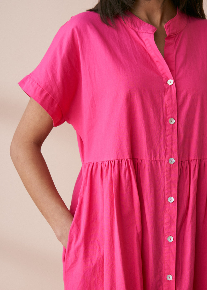 A model wearing a bright pink midaxi shirt dress with short sleeves and mother of pearl buttons