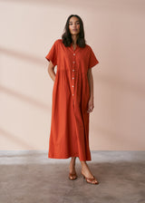 A model wearing a oversized shirt dress in a rusty red tone with mother of pearl buttons