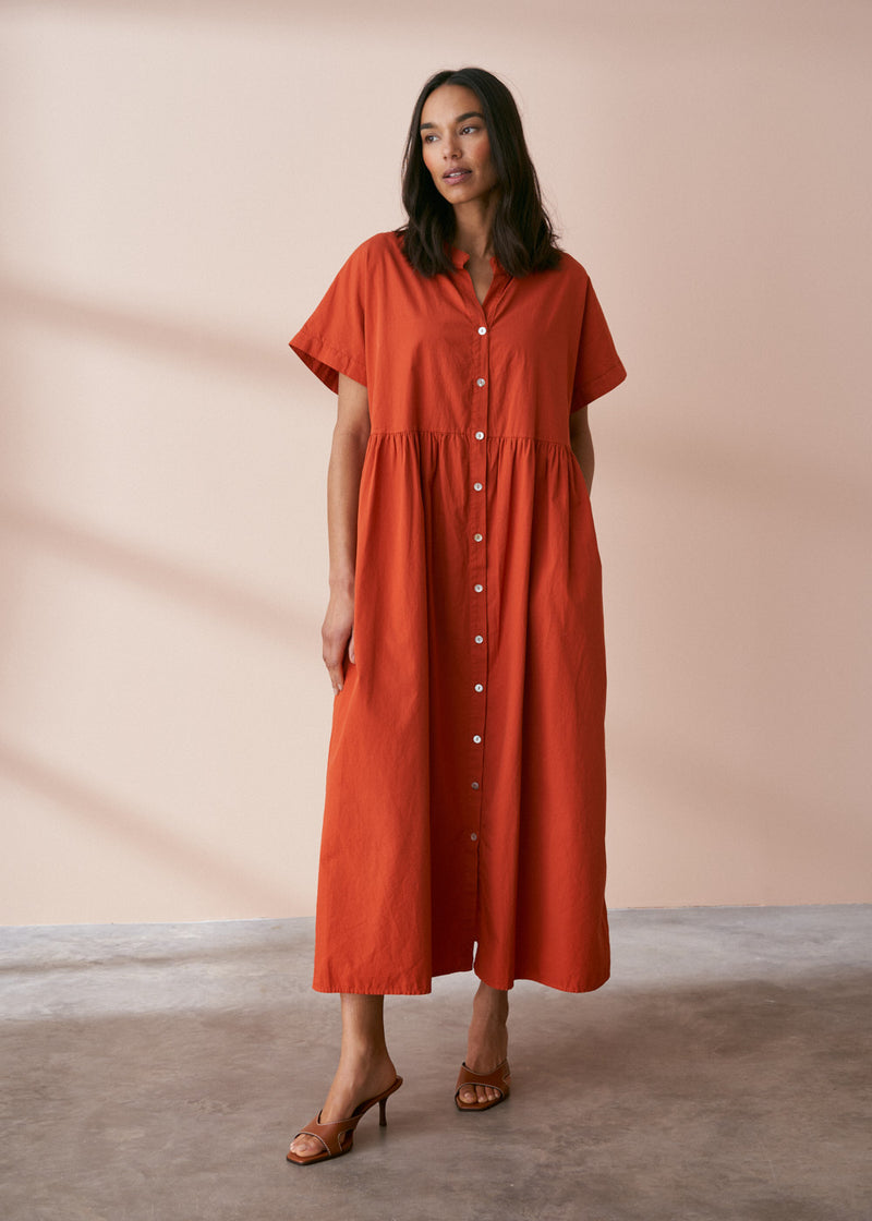 A model wearing a oversized shirt dress in a rusty red tone with mother of pearl buttons