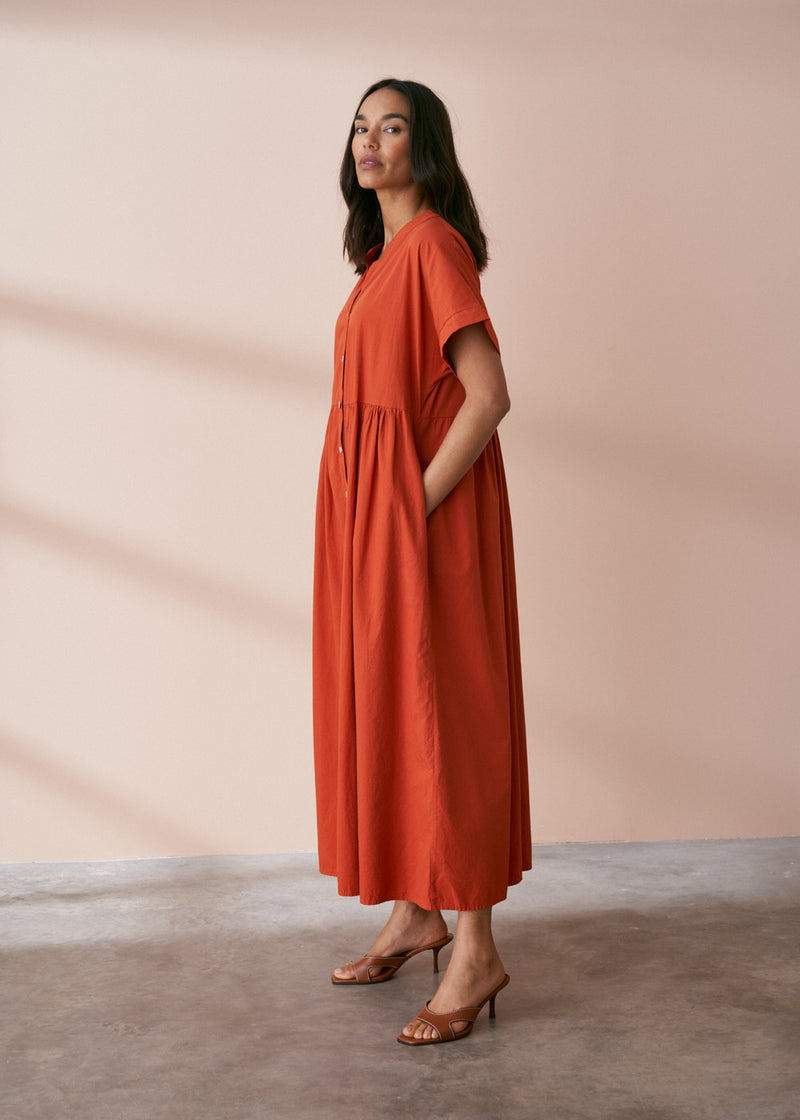 A model wearing a oversized shirt dress in a rusty red tone with mother of pearl buttons