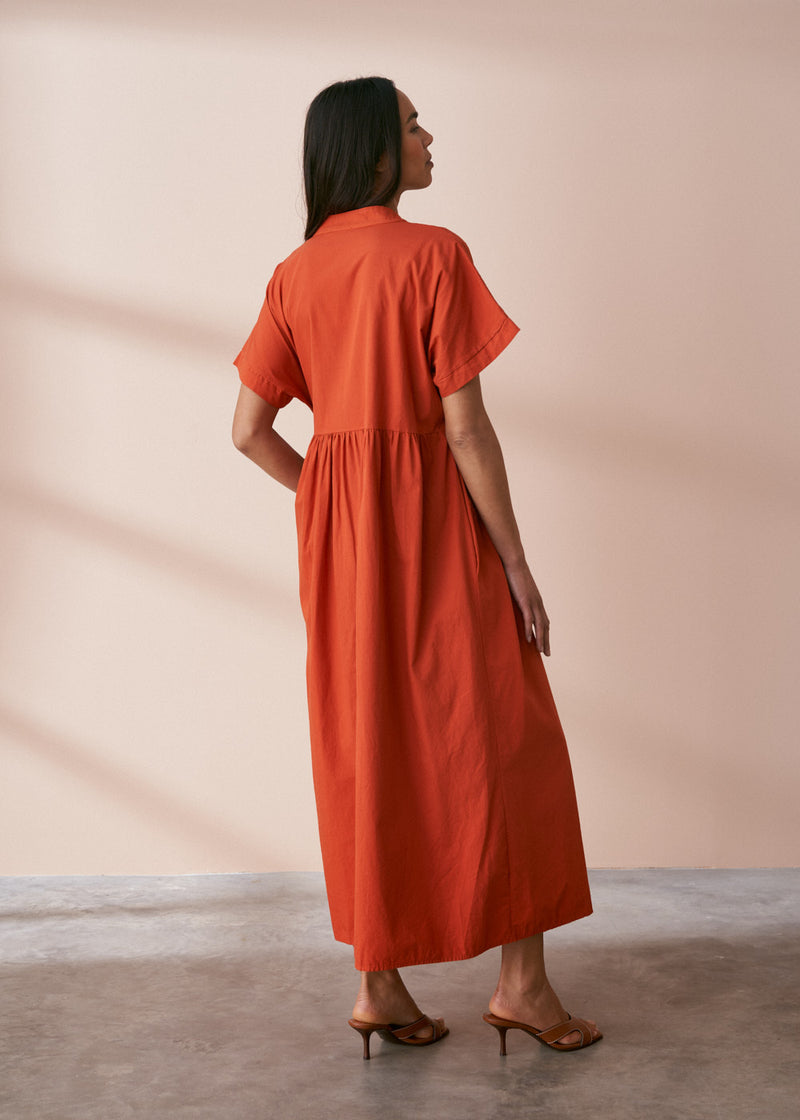 A model wearing a oversized shirt dress in a rusty red tone with mother of pearl buttons