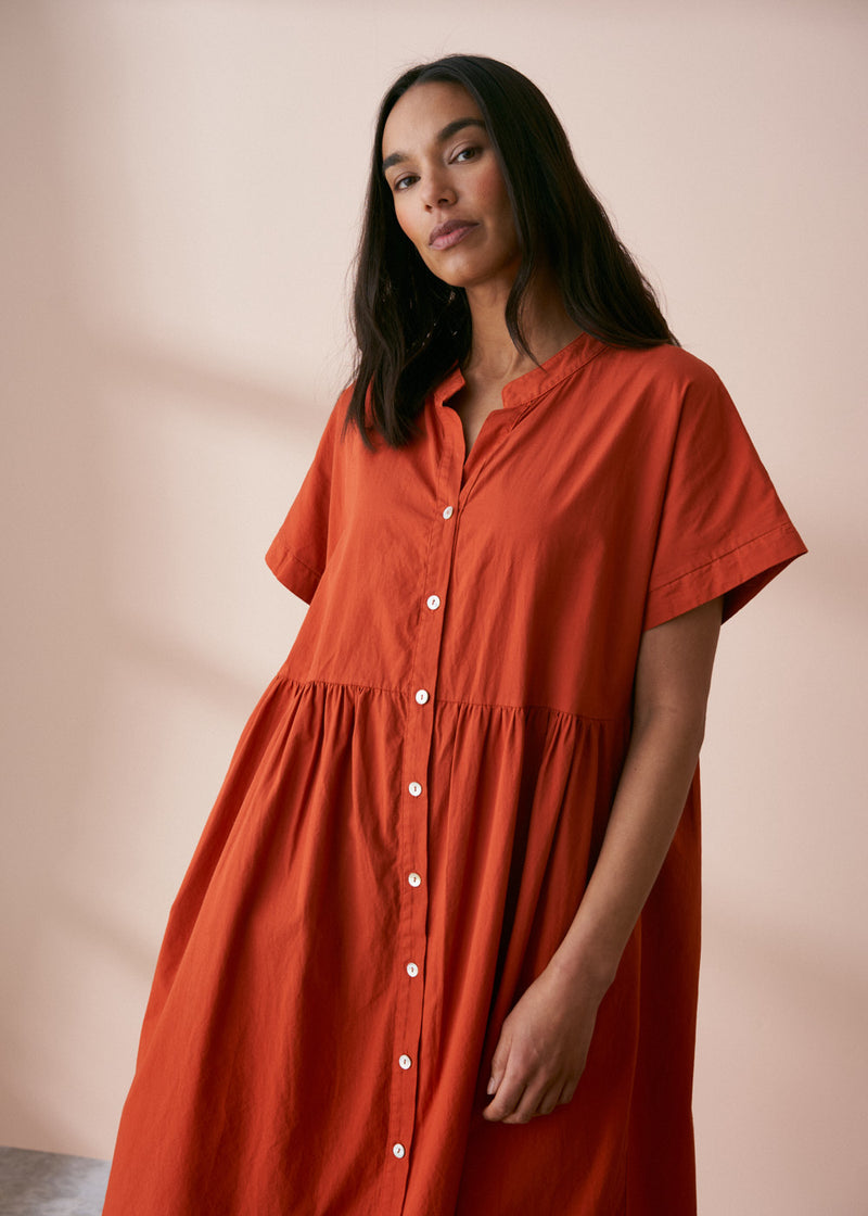 A model wearing a oversized shirt dress in a rusty red tone with mother of pearl buttons