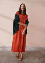 A model wearing a oversized shirt dress in a rusty red tone with mother of pearl buttons