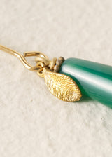 Jewelry with a gold leaf charm and green teardrop pendant on a textured beige background