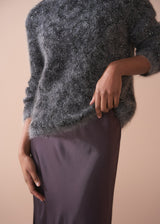 Woman wearing a dark grey fluffy textured sweater with sequin detail.