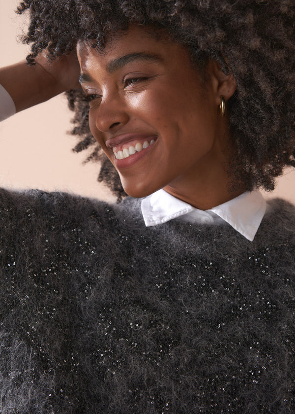 Woman wearing a dark grey fluffy textured sweater with sequin detail.
