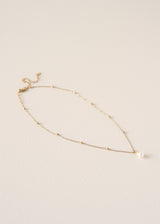 Delicate gold necklace with a single pearl on a beige background