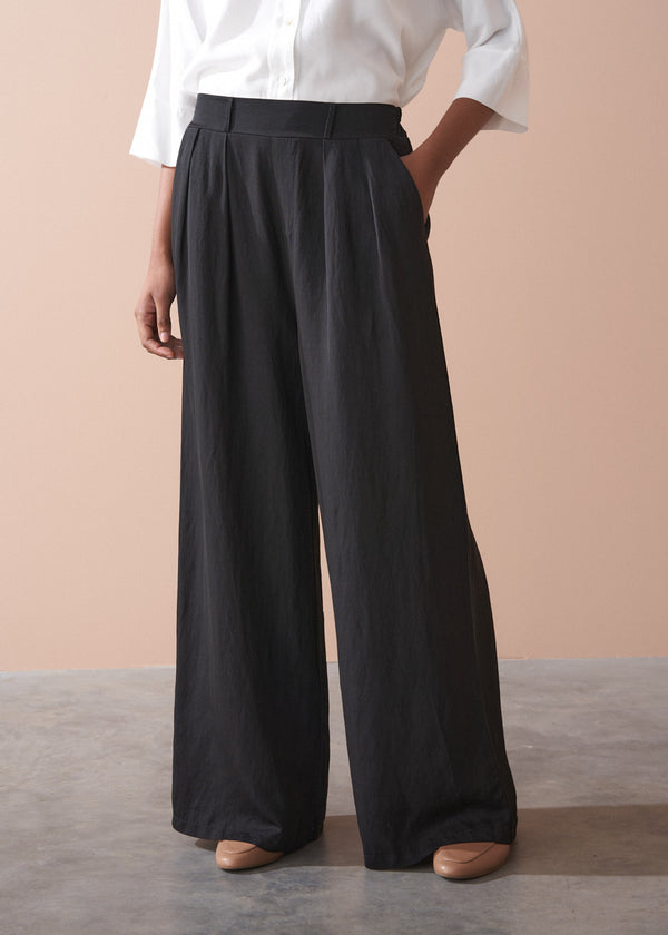 Person wearing black wide-leg trousers and a white shirt against a beige background