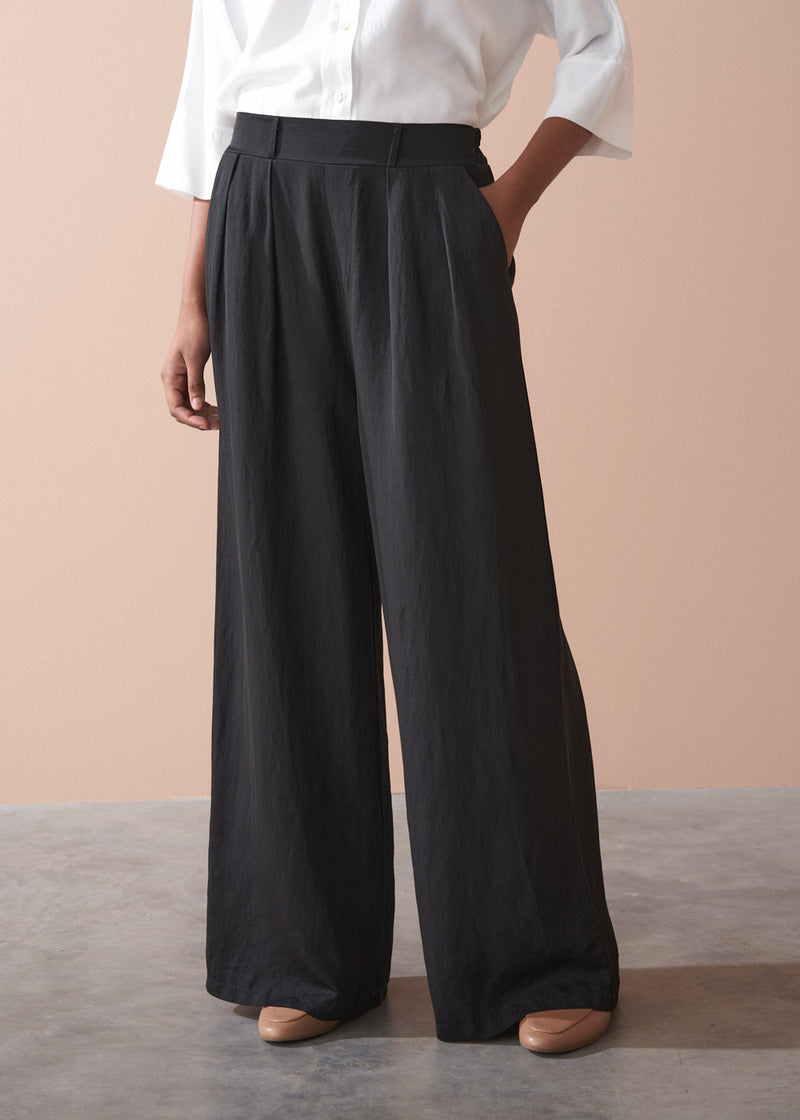 Person wearing black wide-leg trousers and a white shirt against a beige background