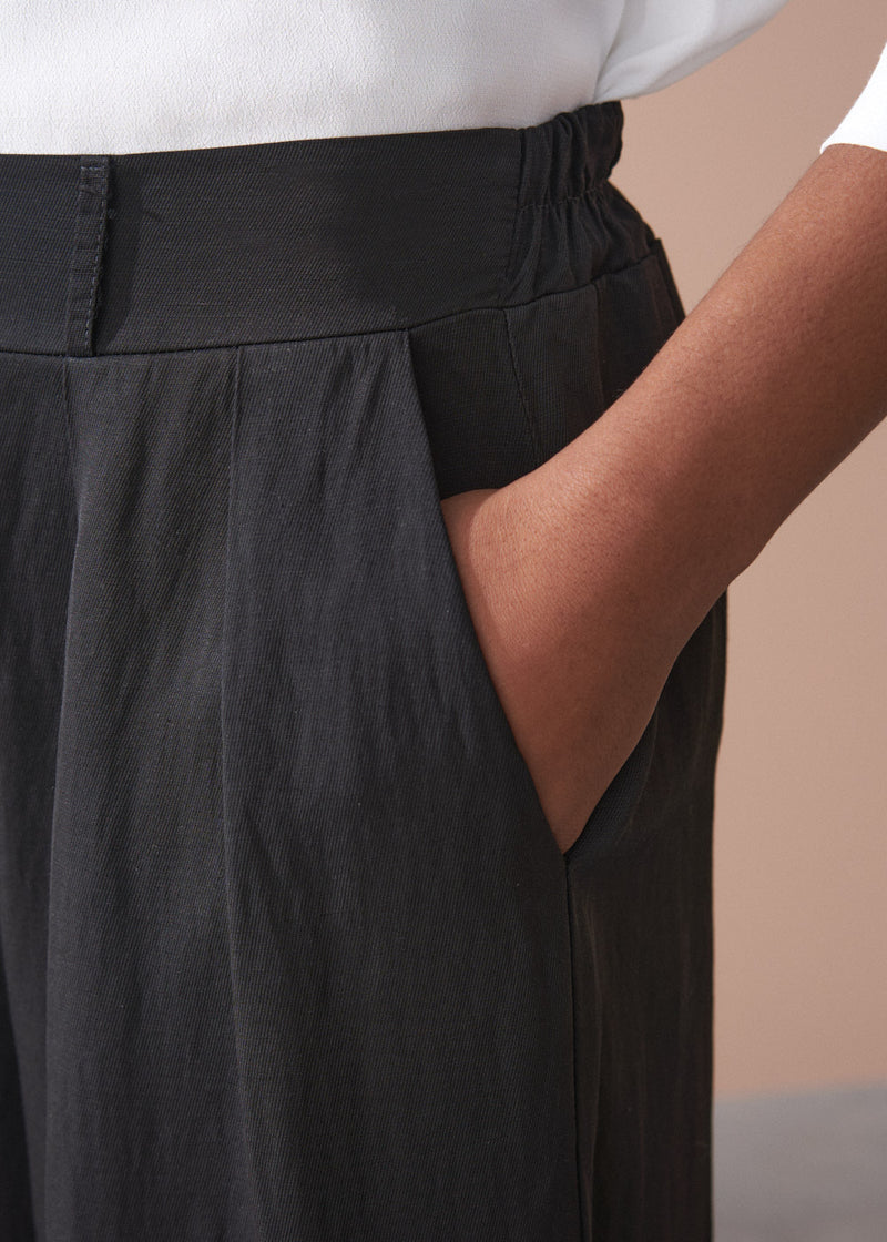 Person wearing black wide-leg trousers with a neutral background