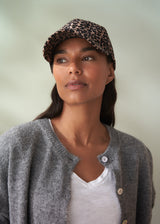 Woman wearing a leopard print cap and gray cardigan against a plain background