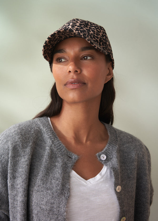 Woman wearing a leopard print cap and gray cardigan against a plain background