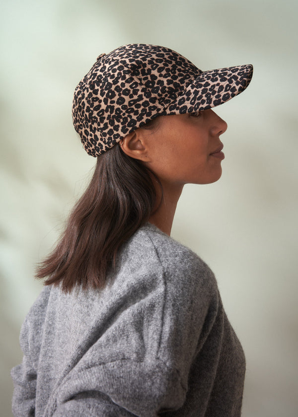 Person wearing a leopard print cap and gray sweater against a neutral background