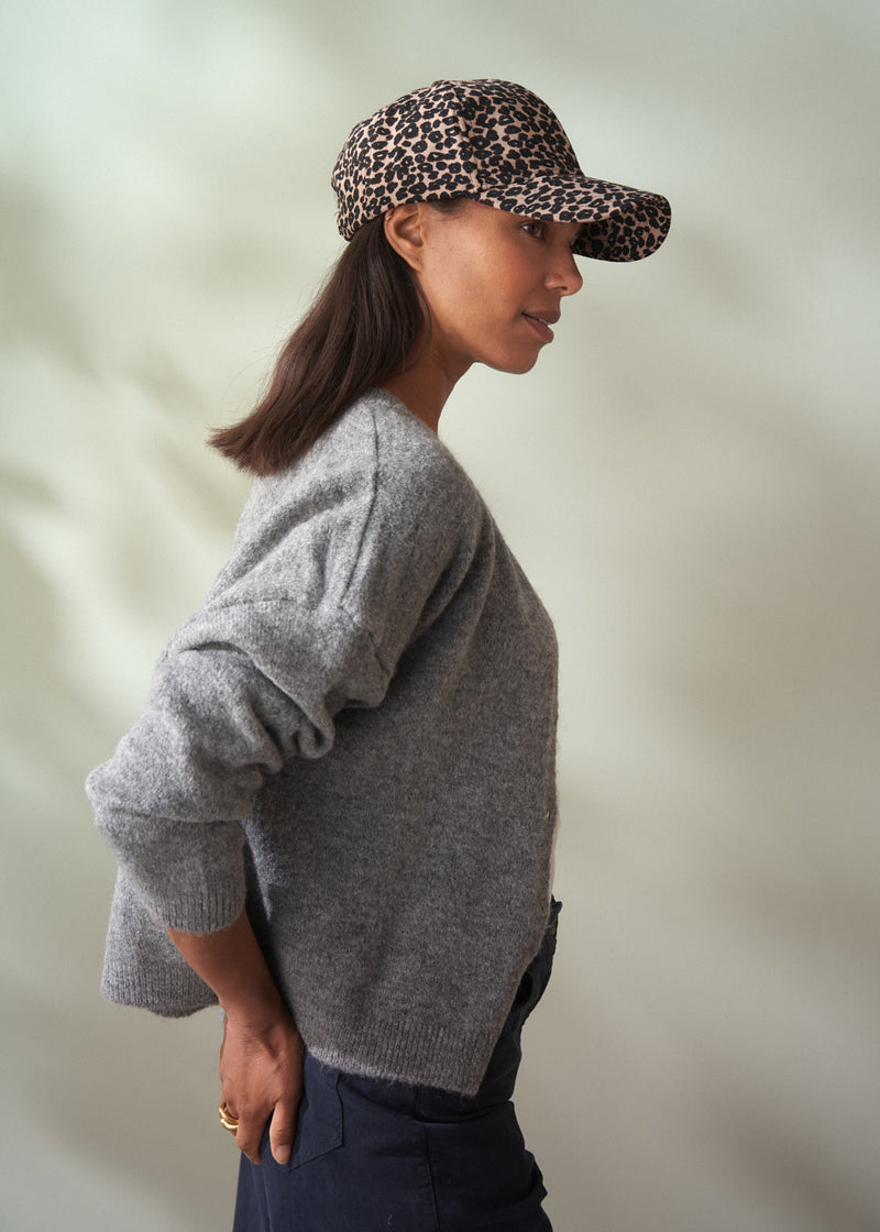 Person wearing a gray sweater and leopard print cap against a neutral background