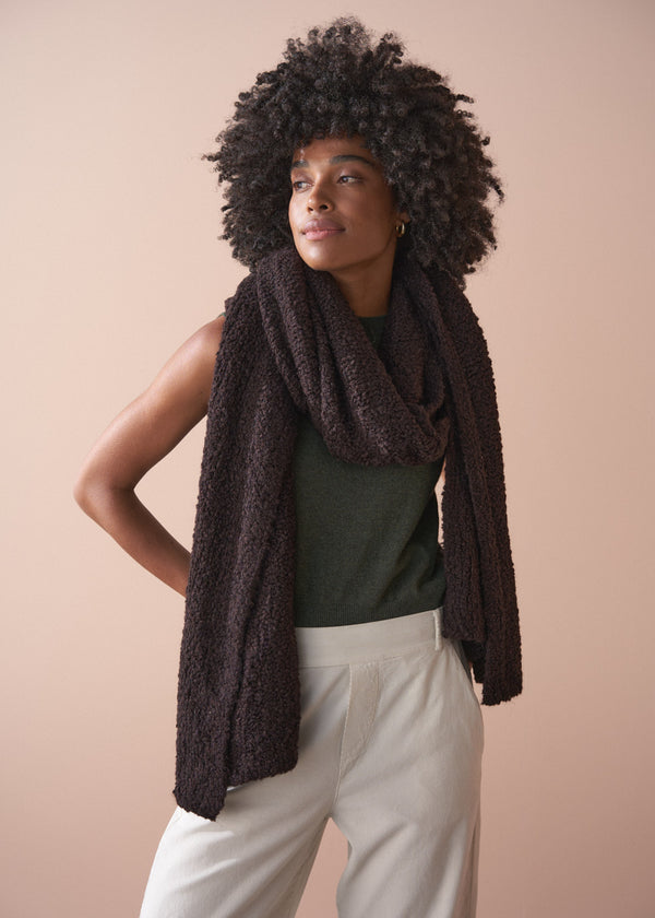 Woman wearing a dark brown knitted scarf against a beige background