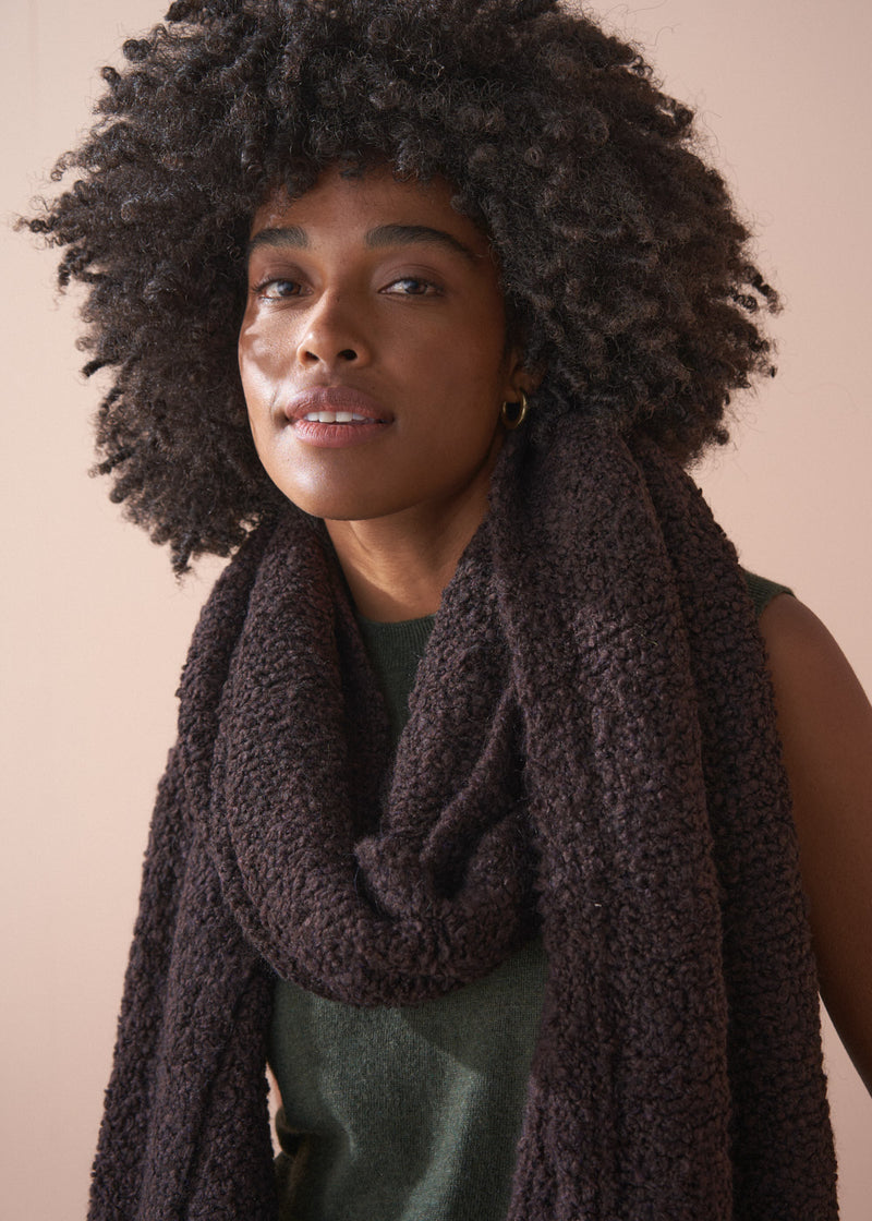 Woman wearing a dark brown knitted scarf against a beige background