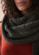 Person wearing a dark green knitted scarf with a blurred background
