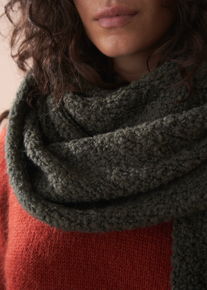 Person wearing a dark green knitted scarf with a blurred background