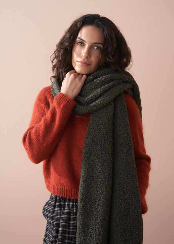 Woman wearing a red sweater and dark green scarf against a beige background