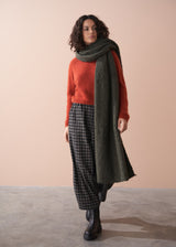 Woman wearing a red sweater, plaid trousers, and green scarf against a beige background