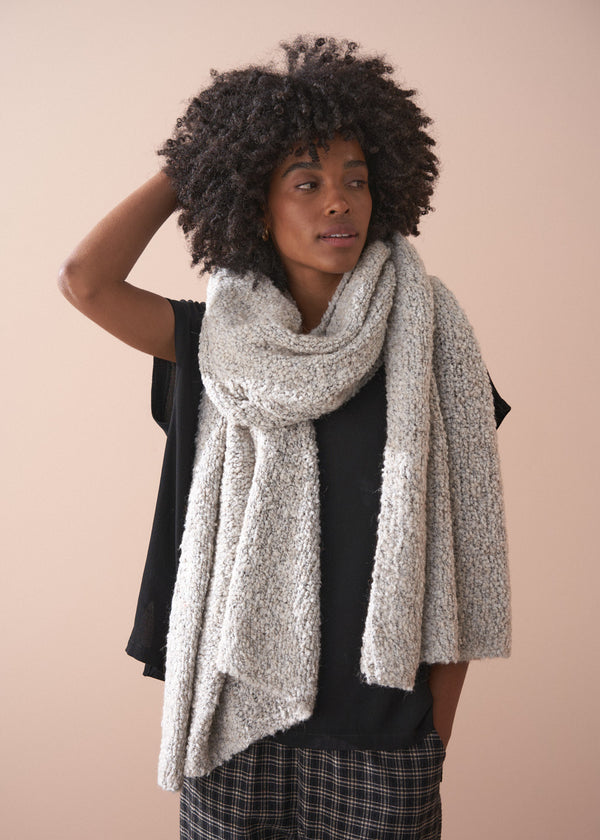 Woman wearing a large beige scarf against a plain background