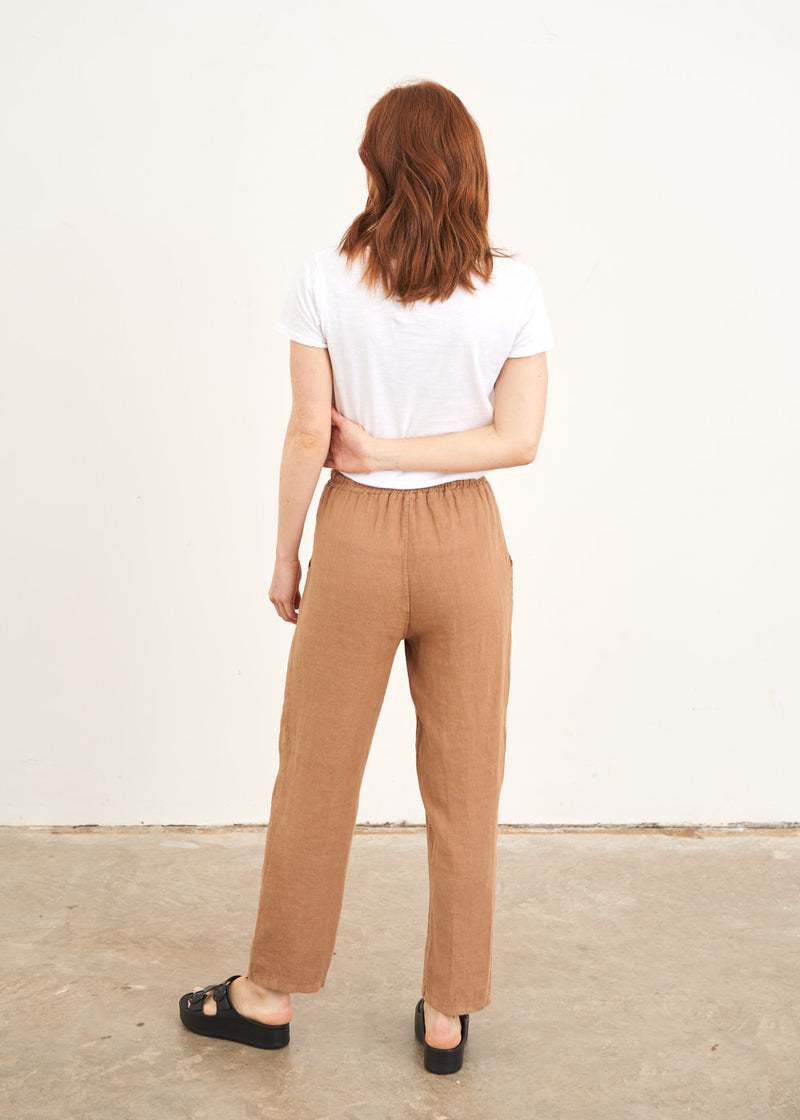 A model wearing a white shortsleeced t shirt with camel coloured straight linen trousers and black slides