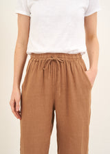 A model wearing a white shortsleeced t shirt with camel coloured straight linen trousers and black slides