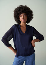 Woman wearing a navy blue blouse with sheer sleeves against a plain background