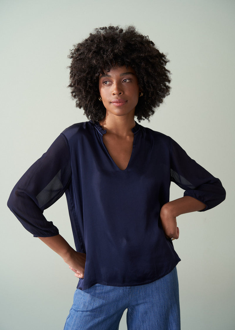 Woman wearing a navy blue blouse with sheer sleeves against a plain background