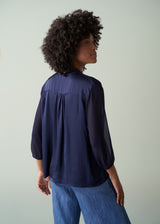 Woman wearing a navy blue blouse and blue pants against a plain background