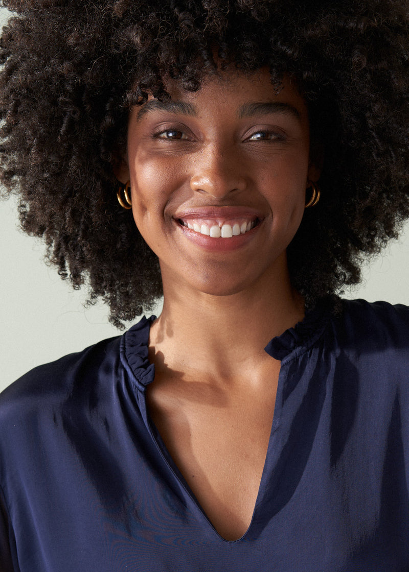 Woman with an afro wearing a navy blue top against a neutral background