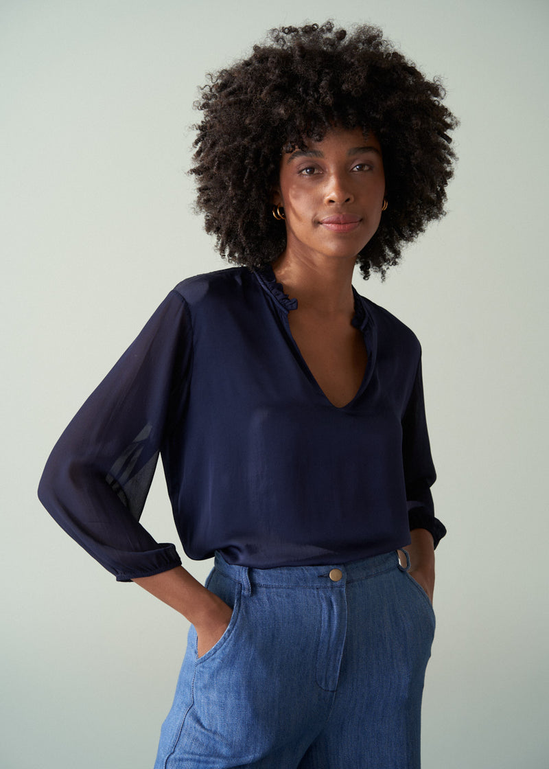 Woman wearing a navy blouse and blue pants against a plain background