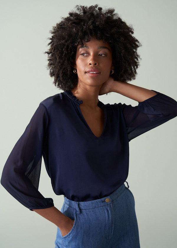 Woman wearing a navy blue blouse and blue jeans against a plain background