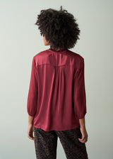 Person wearing a burgundy blouse with a plain background