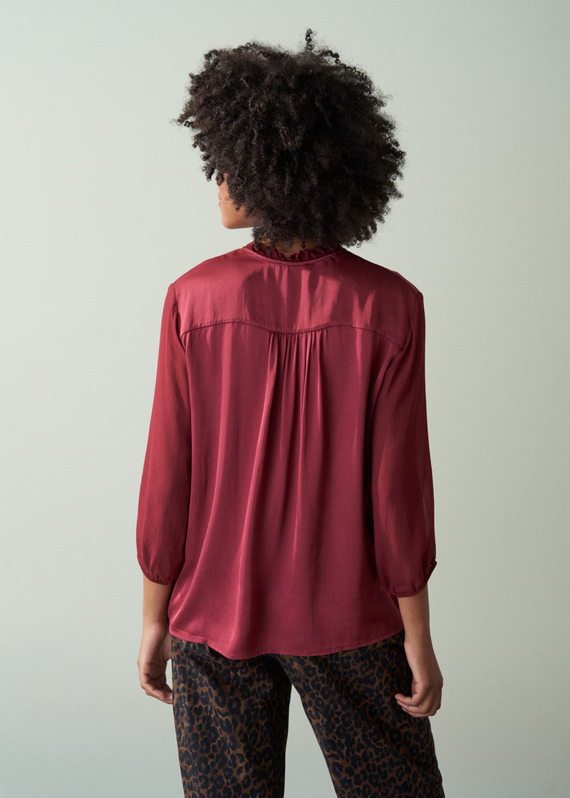 Person wearing a burgundy blouse with a plain background