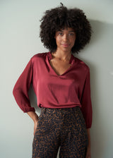 Woman wearing a burgundy blouse and leopard print barrel leg trousers against a plain background