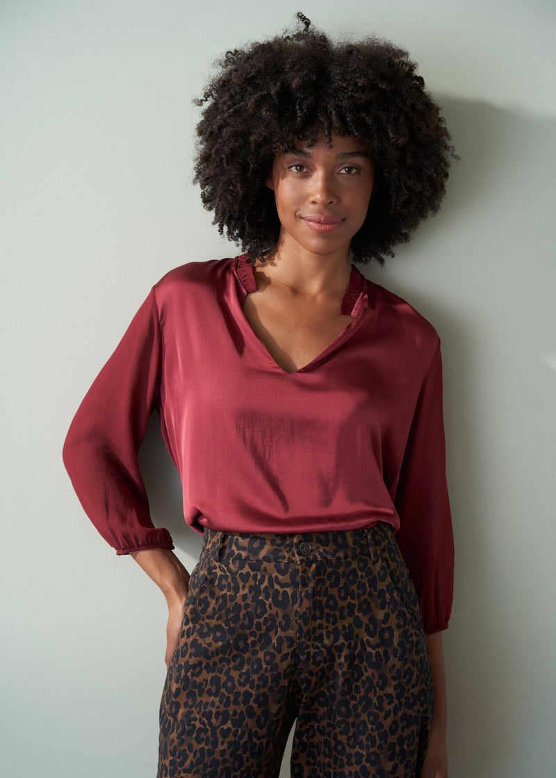 Woman wearing a burgundy blouse and leopard print barrel leg trousers against a plain background