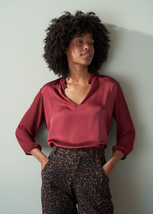 Woman wearing a red blouse and leopard print barrel leg trousers against a light gray wall