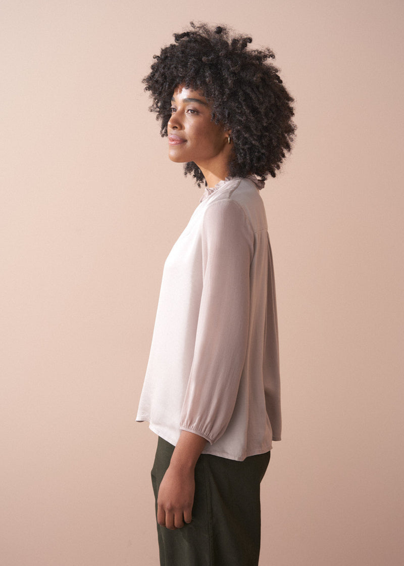 Woman wearing a pale lilac satin  blouse against a beige background